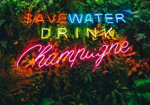 Neon inscription Save water drink champagne. Tropical jungle leaves with neon light lettering.