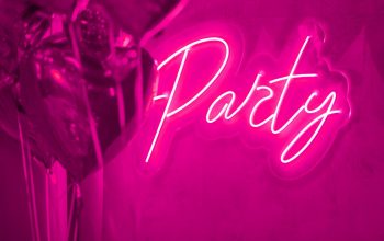 Extravagant bedroom luxury interior with love glamur decoration at Valentines day in studio. Balloons by heart shaped and at illuminated mirror romantic cozy atmosphere at vivid red background. Beautiful place for st Valentine's holiday with neons letters for playboy amore party. Glossy apartment with retro pink signage 80s text lamp shine sign neon style on wall for the sensual nigh. Rich hotel room glamorous elegant modern dream design inside